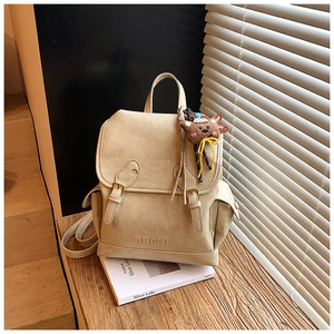 Detail of cream vintage backpack with buckle straps and a small teddy bear charm