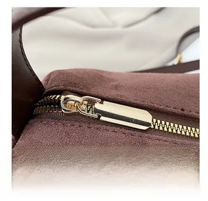 Detailed macro view of a smooth gold metal zipper on a dark brown suede handbag