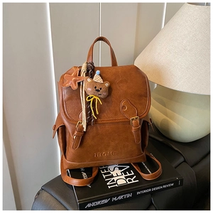 Detail view of a vintage brown leather backpack with logo branding and plush bear charm
