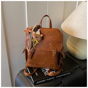 Detailed view of brown retro leather backpack with bear charm and embossed logo detail