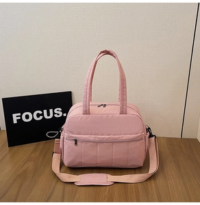 Close-up of pink nylon travel bag with top handles, adjustable strap and front pocket