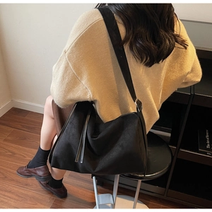 Detail view of large black suede tote bag with wide strap and zipper on a model