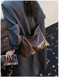 Détail d'un sac cabas marron foncé avec un pompon tressé et une inscription logo dorée