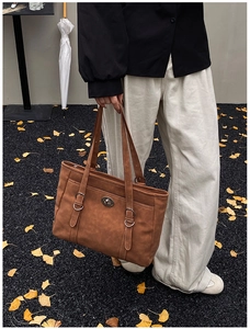 Close-up of vintage brown leather tote bag with silver buckle and autumn ginkgo leaves