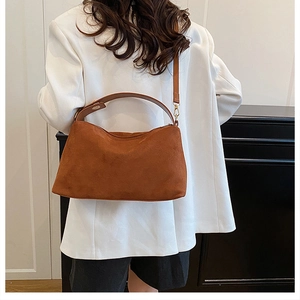 Detail of brown faux suede pillow bag worn over white blazer for a commute look