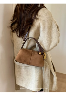 Detail of caramel suede pillow bag with large gold buckle and brown leather handle
