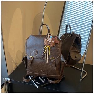 Detail of vintage brown leather backpack with embossed logo and plush bear charm