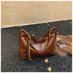 Détail d'un sac hobo marron caramel avec pompon tressé sur un sol en galets noirs