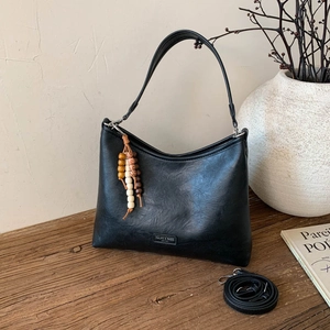 Close-up of black matte shoulder bag featuring a wooden bead pendant and a logo detail
