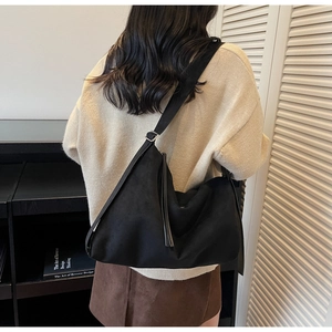 Detail of a large black suede crossbody bag with wide strap and silver metal buckle