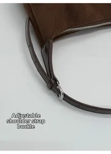 Detail of adjustable shoulder strap with silver buckle on brown suede underarm bag