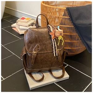 Detail view of brown vintage leather backpack with bear charm and brand logo embossing