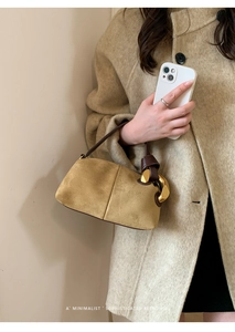 Detail of a ginger suede Boston bag with a large gold ring handle on a wool coat