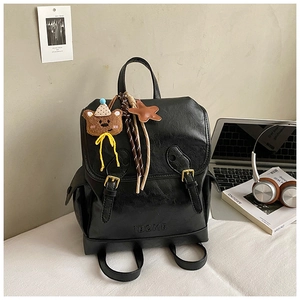 Close-up of black PU leather backpack with gold buckle straps and cute teddy bear charm