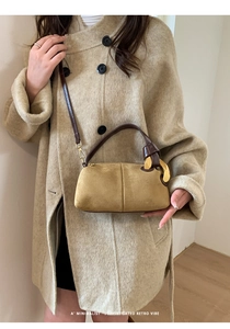 Detail of mustard suede Boston bag with gold rings and brown leather strap on beige coat