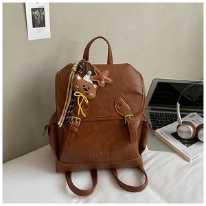 Detailed view of brown faux leather backpack with metallic buckles and plush bear pendant