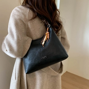 Detail of black semi-circle leather bag featuring unique bohemian wooden bead tassel