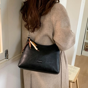 Detail of black hobo bag with colorful bead tassel on model in cream wool coat