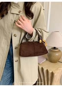 Close-up of brown suede handbag featuring a unique gold metal handle and vintage stitching