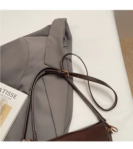 Detail of dark brown glossy leather saddle bag strap on a grey blazer outfit