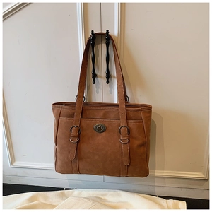 Detail of a brown leather tote bag featuring decorative straps and a vintage metal twist lock