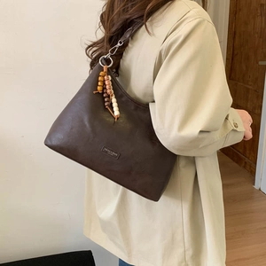 Detail of vintage brown tote bag with beaded tassel and embossed brand logo on PU leather
