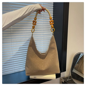 Detail of khakhi suede tote bag featuring a decorative woven rope and wooden bead handle