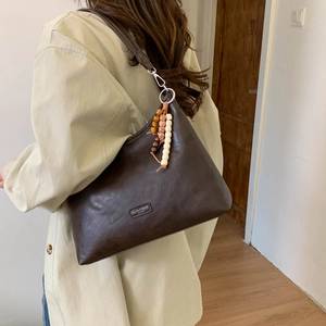 Detailed view of dark brown leather hobo bag featuring ethnic wooden bead pendant charm