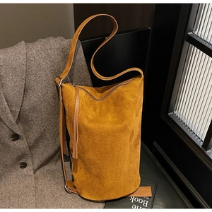Detail of yellow suede bucket bag with leather tassels on a stylish black chair
