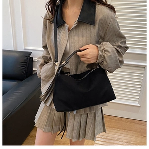 Chic black nylon crossbody pillow bag shown on model wearing a striped jacket