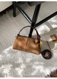 Detail view of brown suede Boston bag with gold buckle on textured carpet backdrop