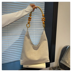 Detail of off-white leather tote bag featuring wooden beads and gold ring hardware
