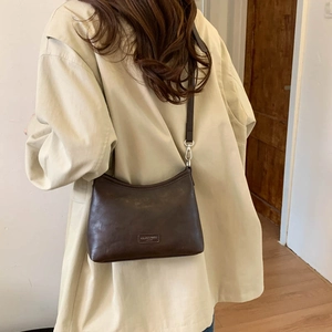 Detail of dark brown leather crossbody bag with brand logo and adjustable strap