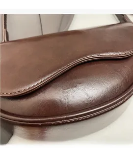 Detail of dark brown saddle bag featuring smooth leather texture and golden lettering