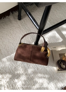 Close-up of dark brown suede Boston bag with golden metal hardware on a white rug