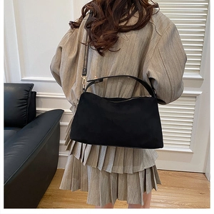 Detail of minimalist black matte crossbody bag with wide strap on brown trench coat