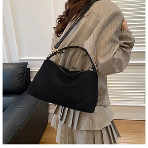 Close-up of black suede tote bag with gold hardware worn by model in modern room