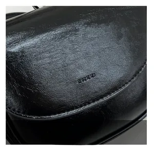 Close-up of black oily wax leather texture and logo stitching on the saddle bag