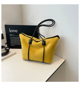 Detail of yellow suede tote bag featuring black woven handles and minimalist design