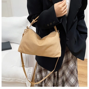 Close-up of beige suede hobo bag with adjustable straps on a stylish model's outfit