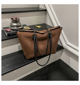 Detailed shot of brown suede tote bag with black braided leather handle on a textured step
