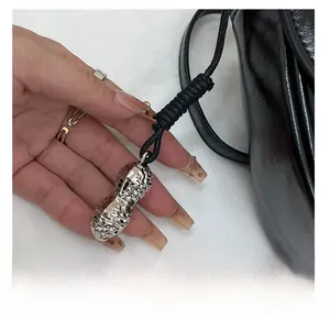 Detail of silver peanut-shaped metal charm with woven rope on a black leather handbag