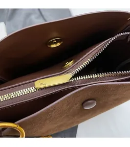 Detail of golden zipper and smooth magnetic buckle on deep brown suede bucket bag