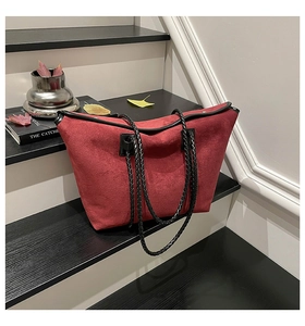 Detail of red suede tote bag with black woven straps and silver rivets on a wooden step
