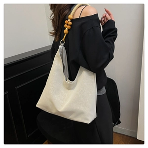 Detail of cream shoulder bag with unique wooden bead strap accents and textured finish