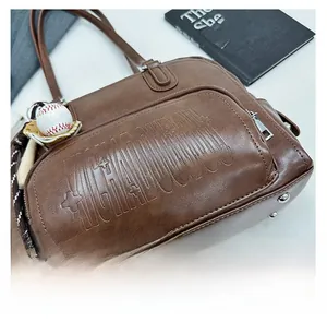 Detail of vintage brown tote bag with embossed lettering and baseball charm ornament