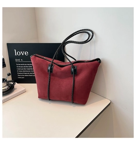 Detail of red frosted suede tote bag with black braided rope handles on light surface