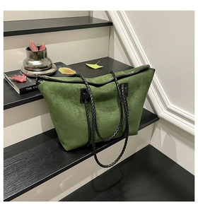 Detail of green suede tote bag with black woven handles on dark wooden stairs