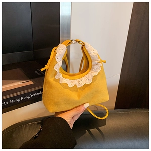 Detail of yellow mini bag featuring white lace embroidery and silver metal handle