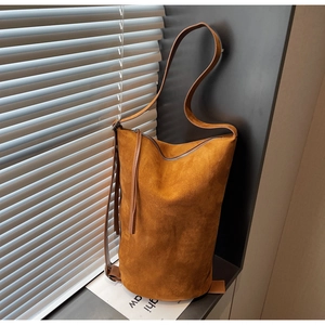 Detail view of brown suede bucket bag featuring silver zipper and slim leather strap